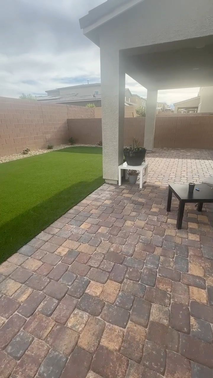 Covered patio with tumbled pavers next to an artificial turf lawn