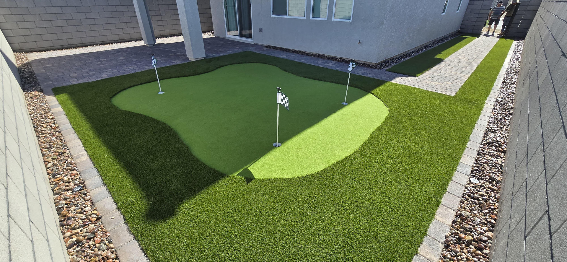 Backyard putting green with three flags bordered by turf and pavers